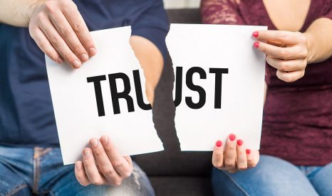 Two people holding a paper with the word "Trust" torn in two