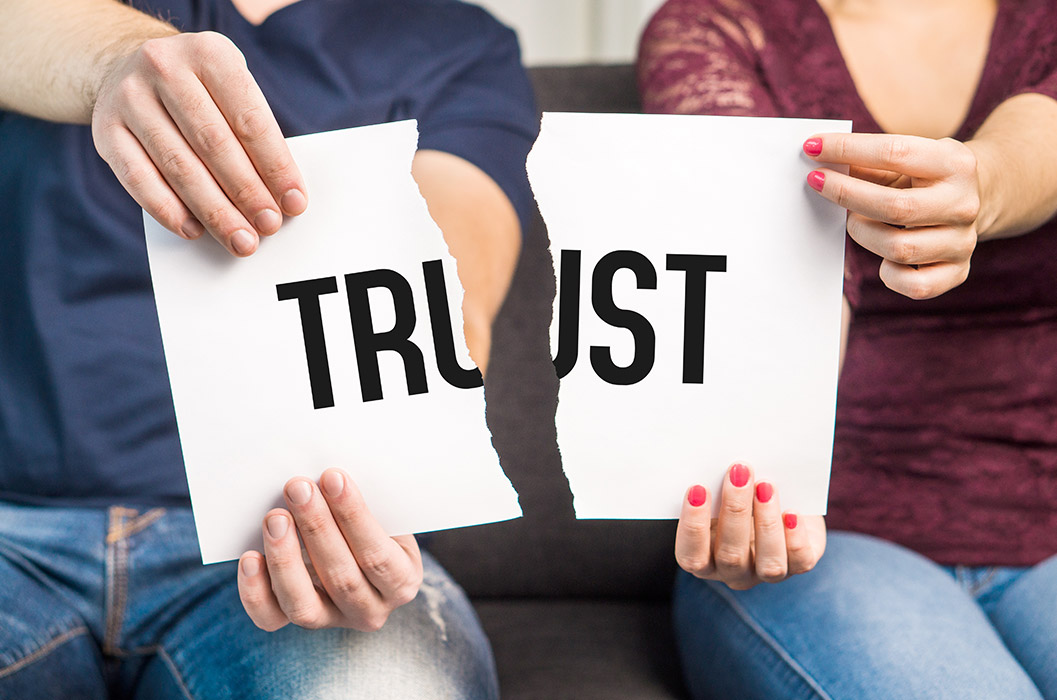 Two people holding a paper with the word "Trust" torn in two