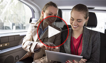 Two women smiling in the backseat of a car watching a tablet